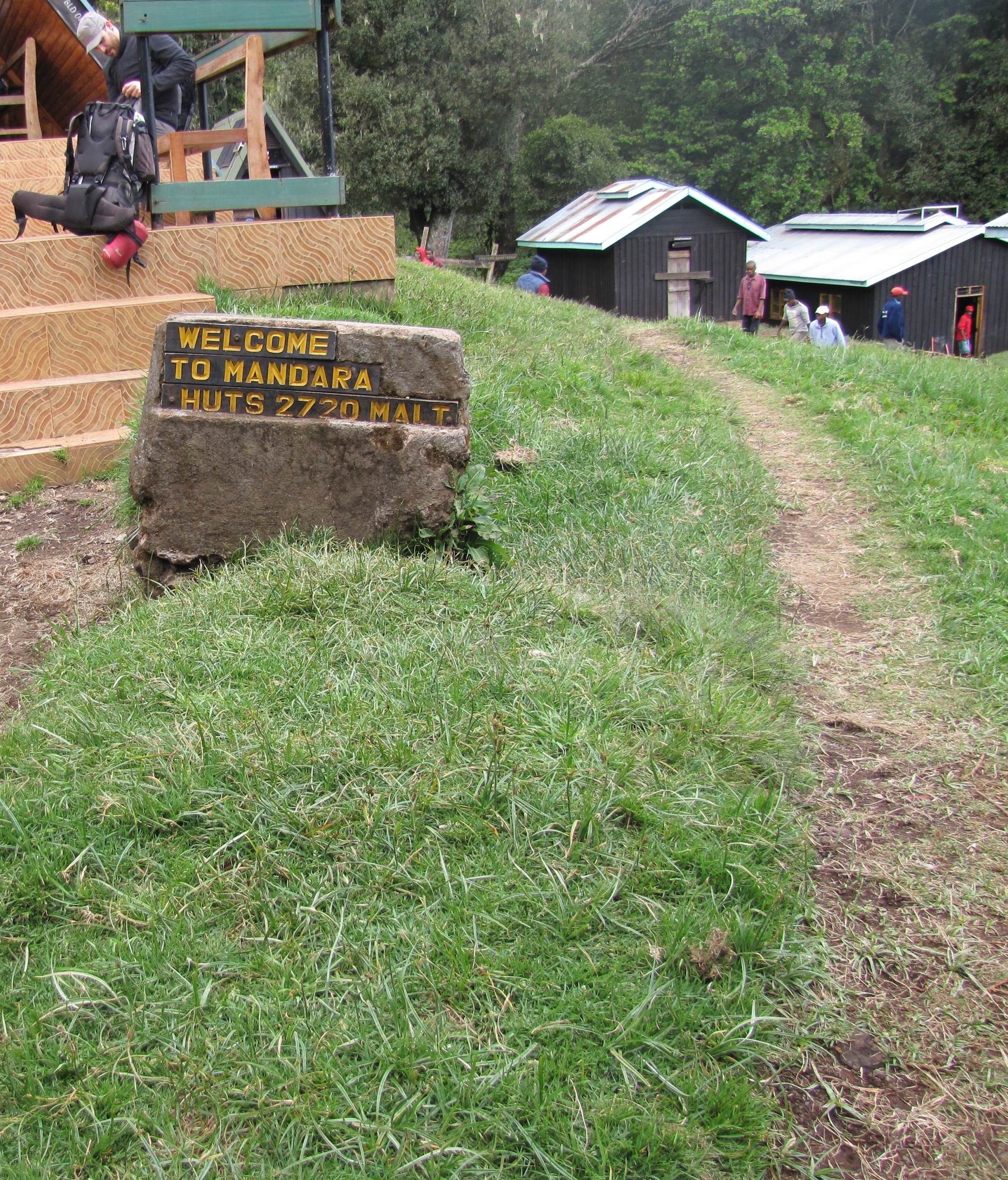 A stone sign reading Welcome to Mandara Huts beside a grassy path