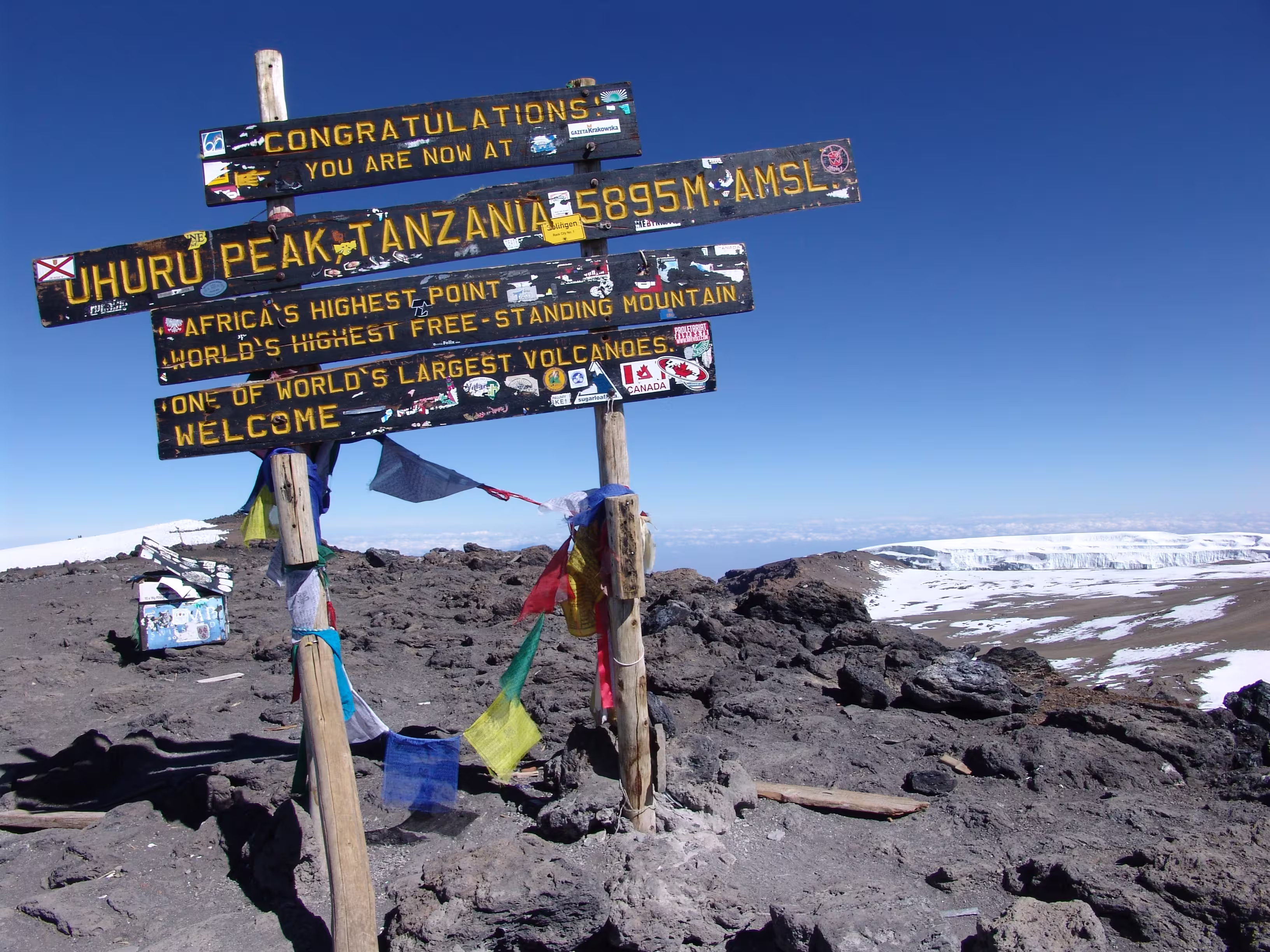 The wooden Uhuru Peak summit sign with prayer flags and glacier ice behind