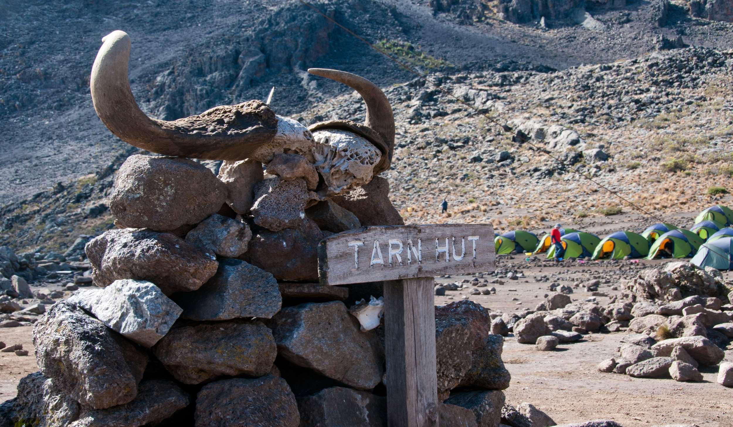 A stone cairn topped with buffalo horns and a Tarn Hut sign, with tents behind