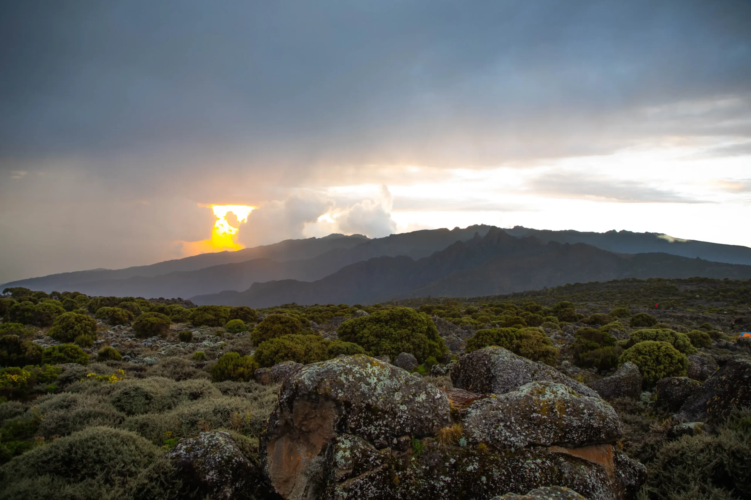 Evening sun breaking through cloud over heath and boulders