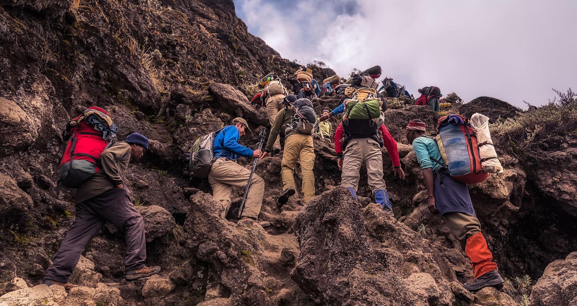 A line of climbers with daypacks scrambling up a steep rock face